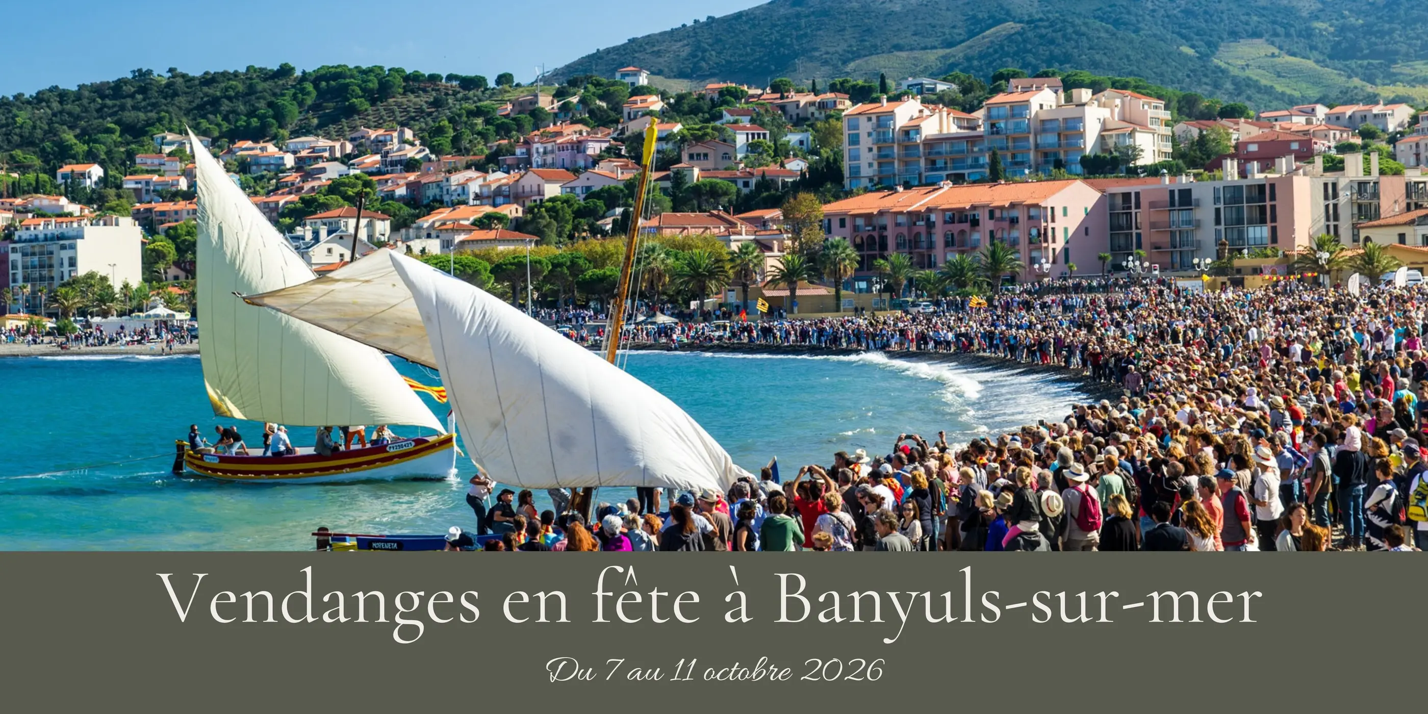 Un voilier navigue près d'une côte où une foule assiste à un événement, avec des bâtiments et des collines en arrière-plan