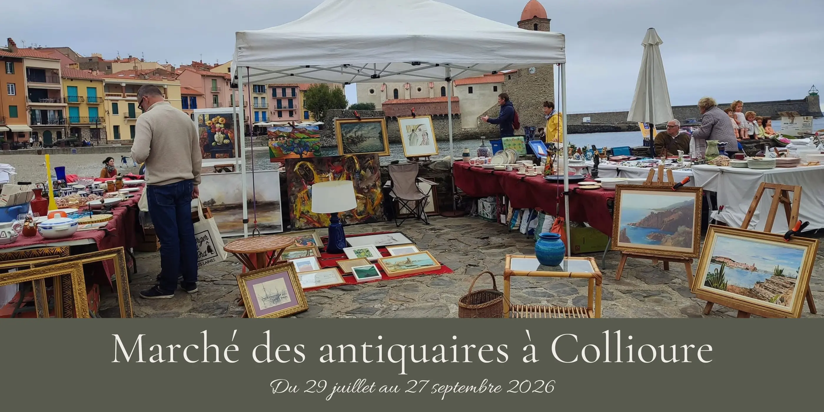 Un marché d'antiquaires à Collioure avec des peintures, des lampes et des objets anciens exposés sous une tente et en plein air, avec des gens qui regardent et discutent
