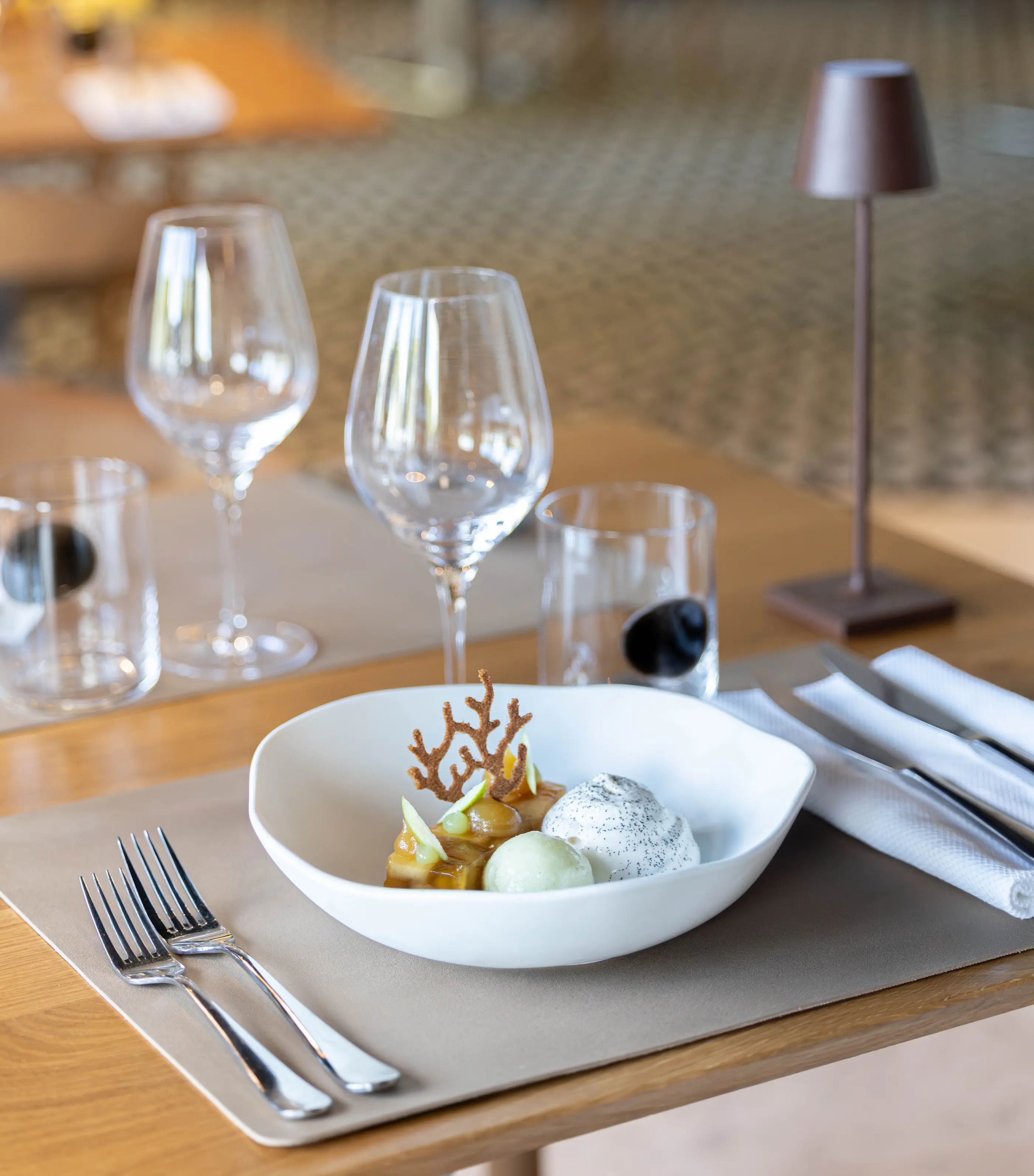 Une assiette de dessert avec des boules glacées, des fruits et une décoration en sucre sur une table dressée avec des verres et des couverts