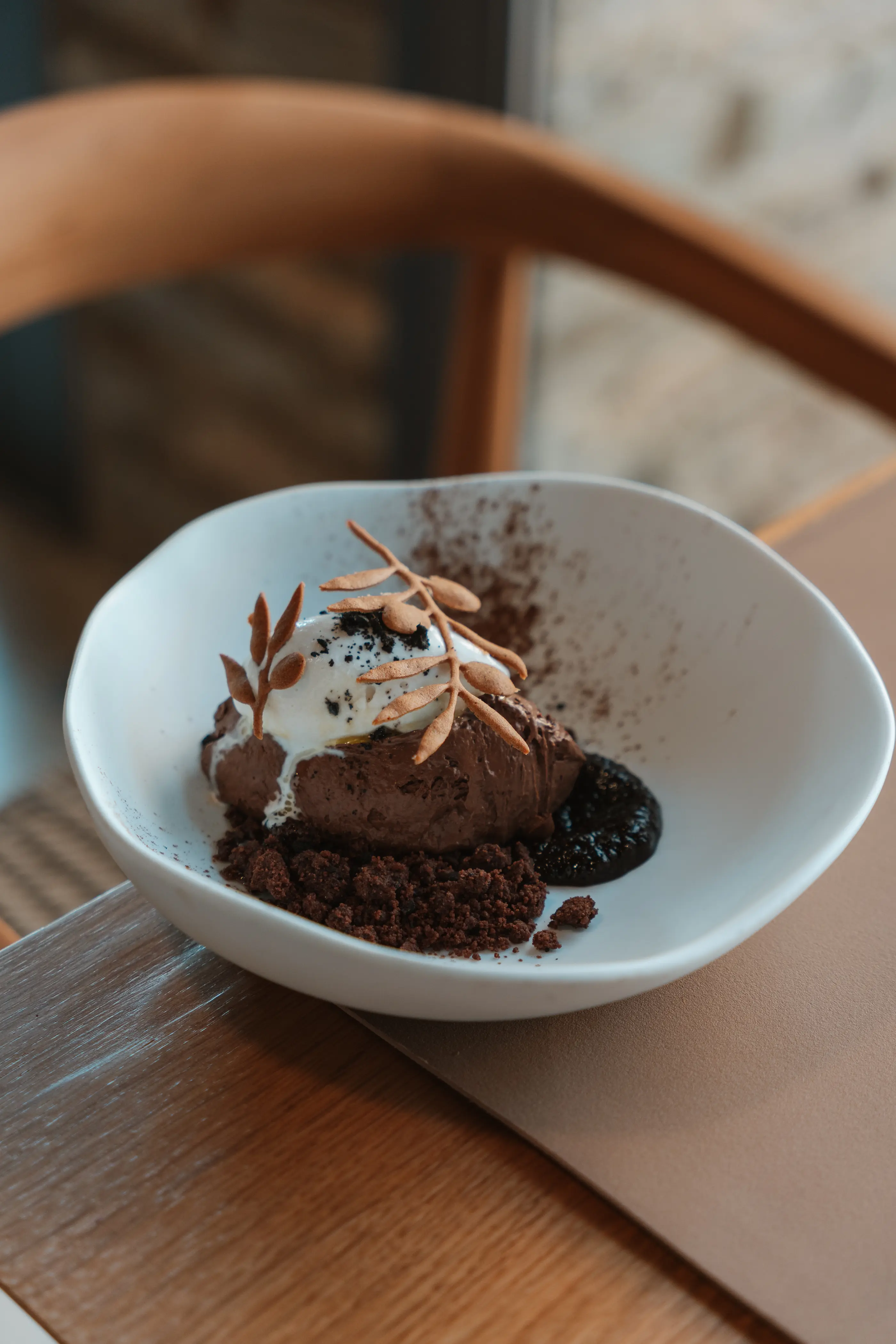 Un dessert au chocolat dans un bol blanc, garni de crème chantilly, de copeaux de chocolat et d'amandes effilées, posé sur une table en bois
