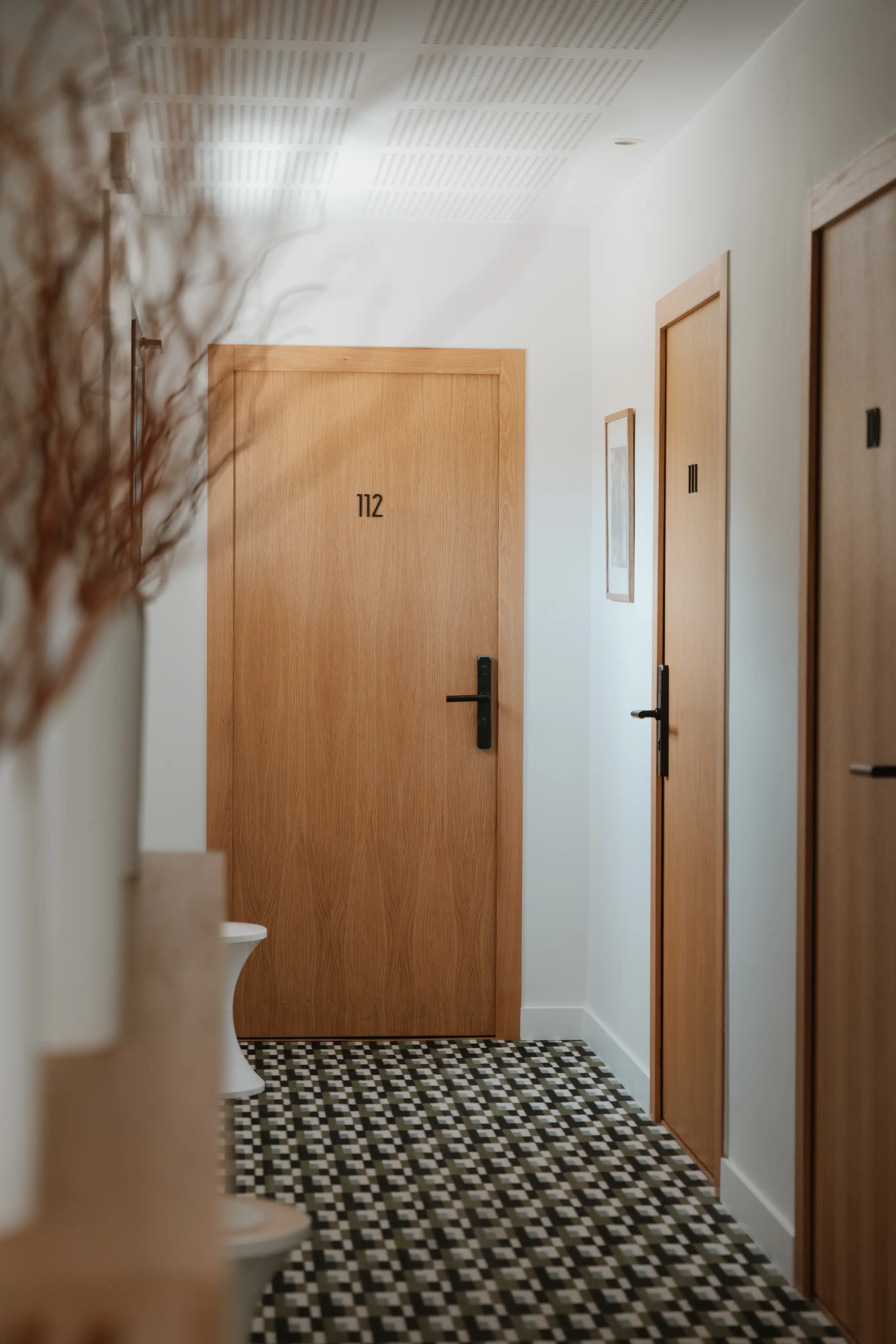 Couloir avec portes en bois numérotées et sol à carreaux noir et blanc