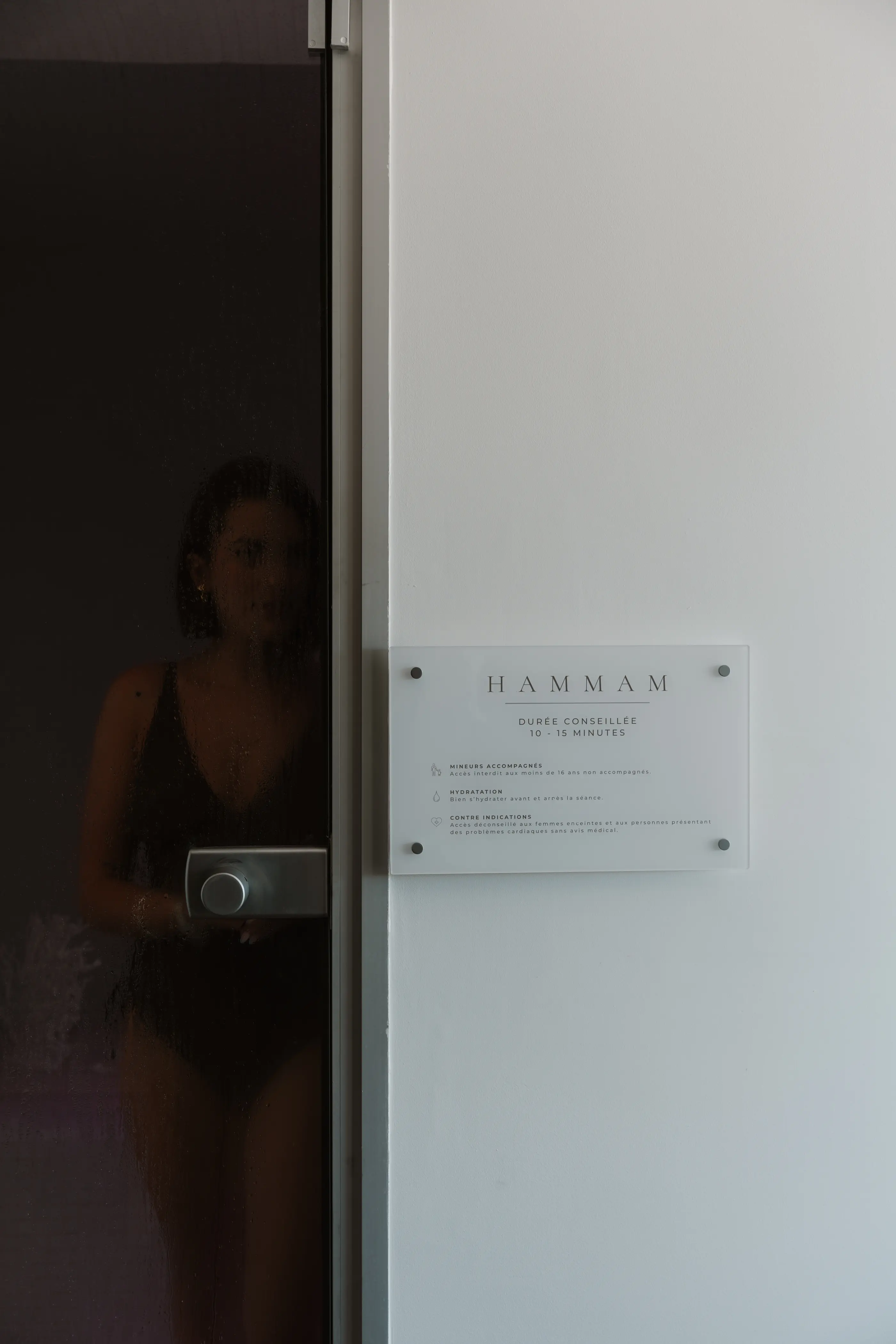 Porte vitrée avec une personne à l'intérieur et une plaque indiquant "HAMMAM" et des instructions en français