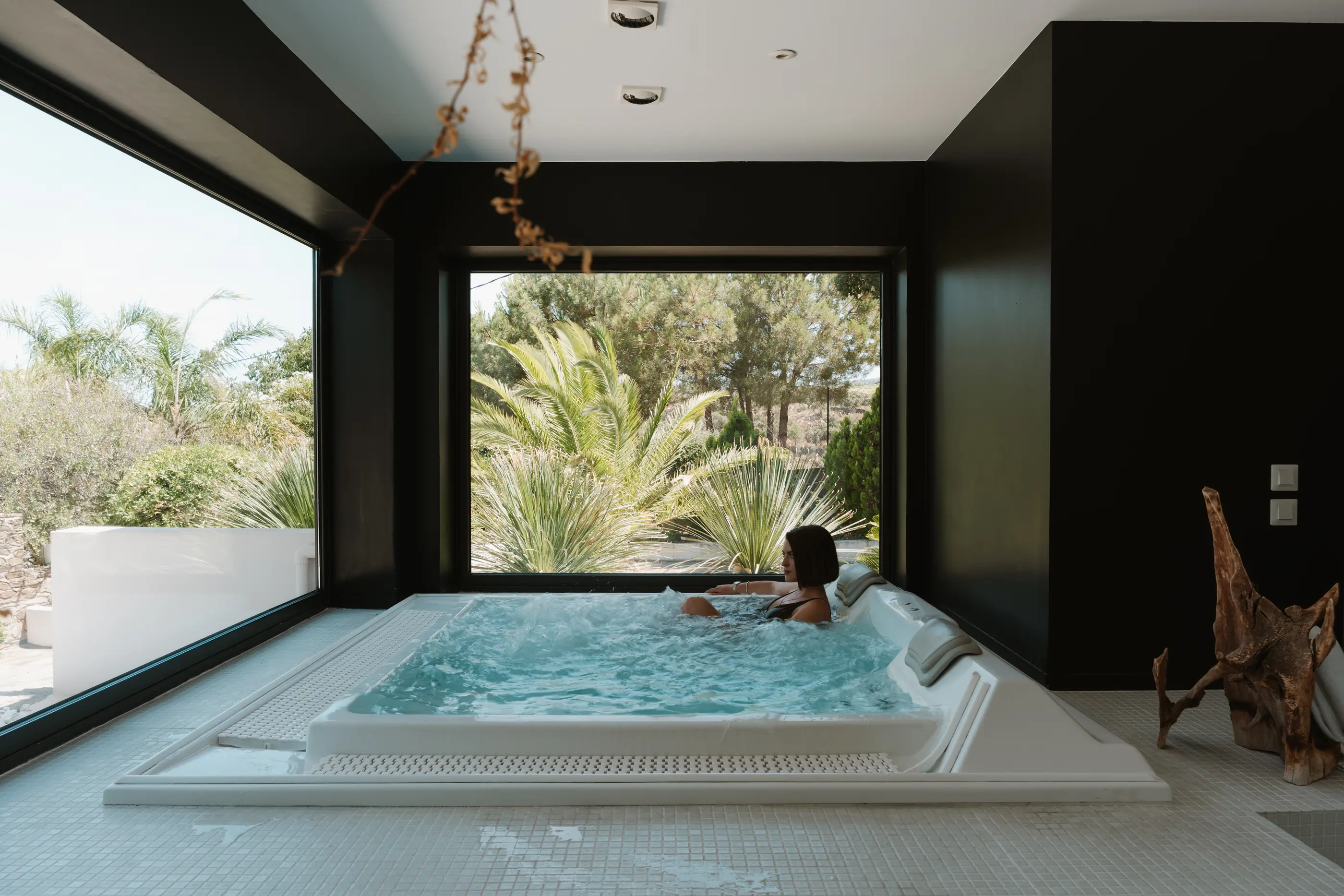 Une personne se détend dans un jacuzzi intérieur avec une grande fenêtre offrant une vue sur un jardin tropical