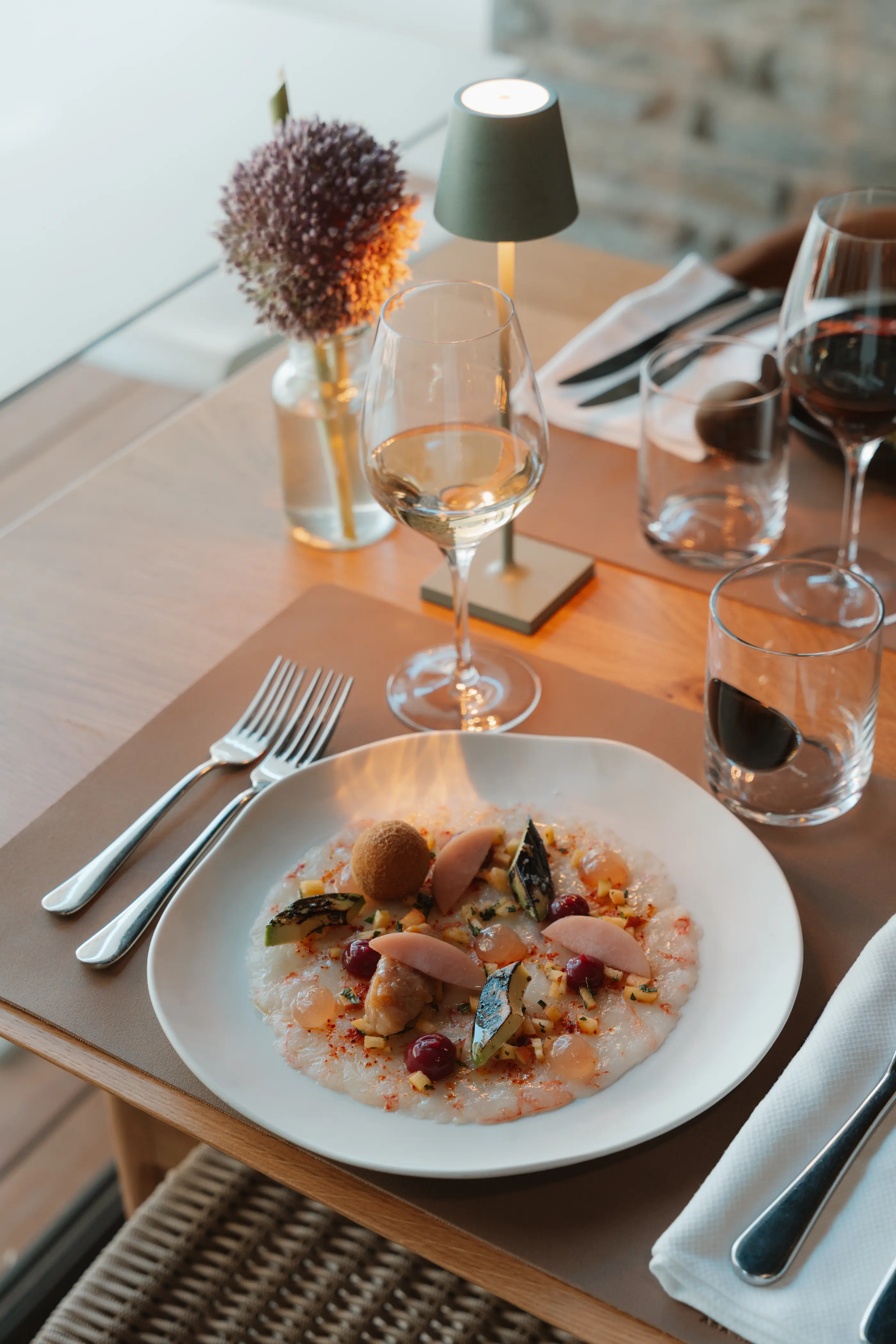 Une assiette de nourriture fine avec divers ingrédients, un verre de vin blanc, des couverts et une décoration florale sur une table en bois