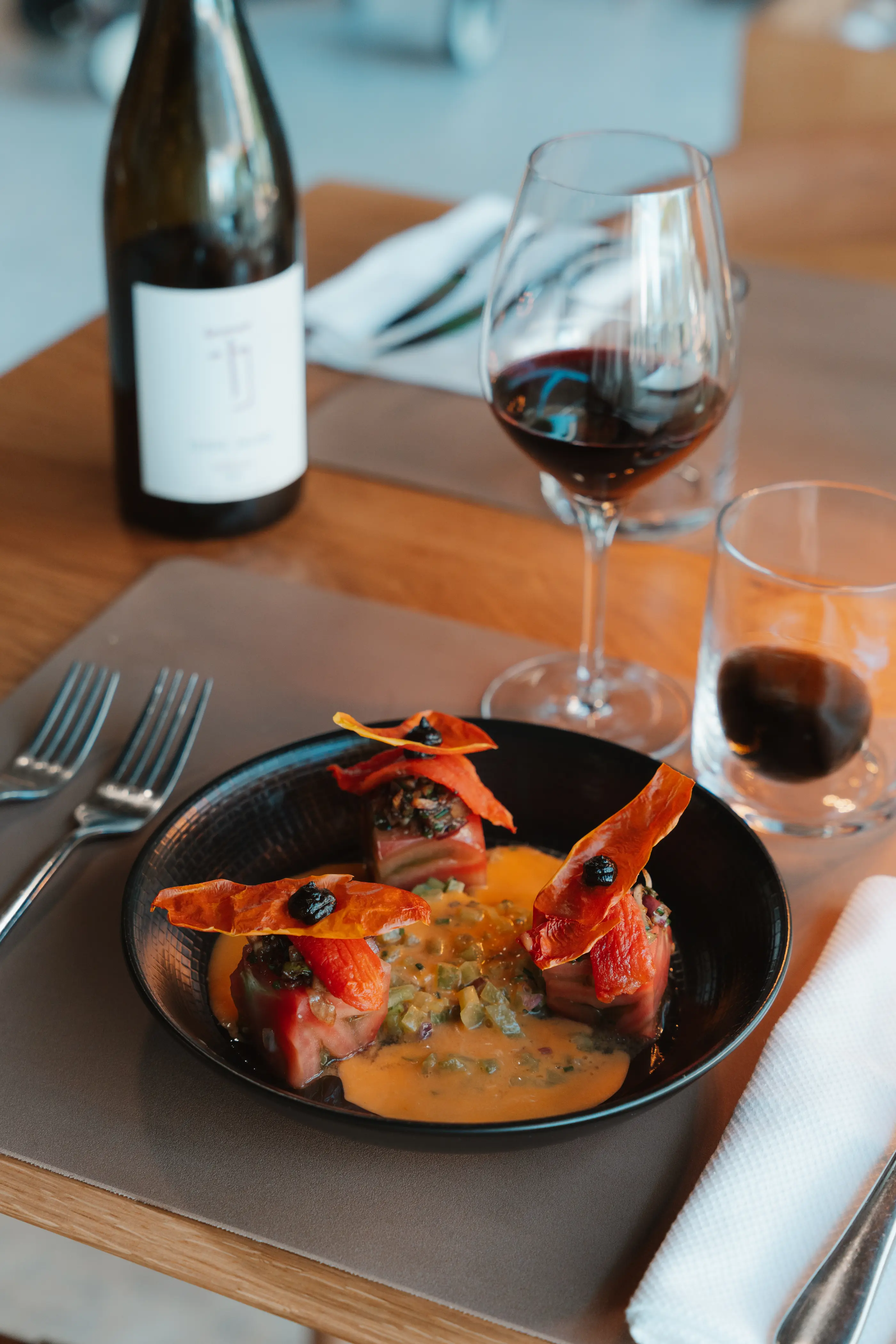Un plat avec des tranches de tomates et de bacon sur une sauce à la crème, accompagné de deux verres de vin rouge et d'une bouteille de vin