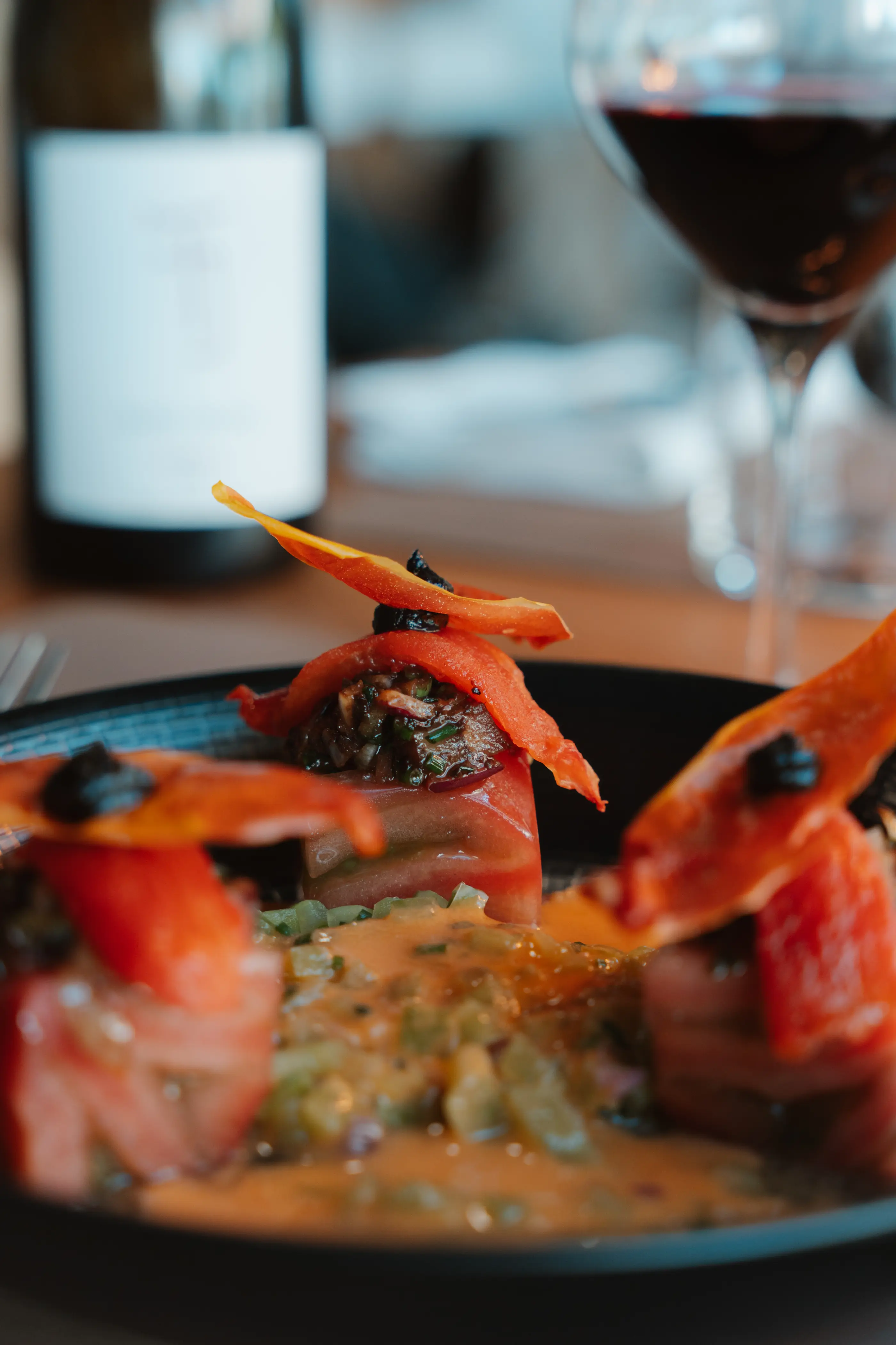 Un plat de pâtes garnies de sauce tomate, d'olives et de carottes, accompagné d'un verre de vin rouge