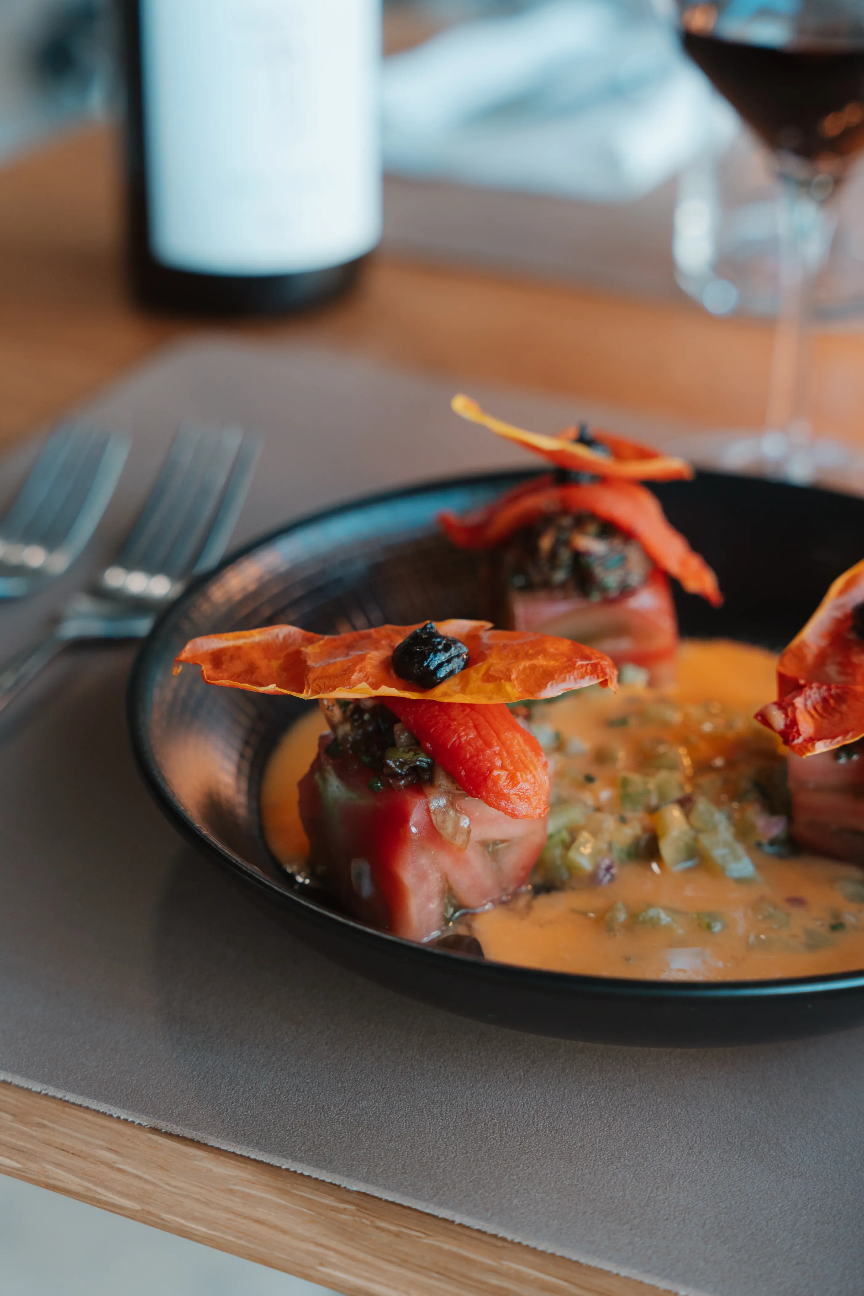 Un plat avec des tomates séchées et une sauce à base de tomates sur une assiette noire, accompagné d'un verre de vin et d'une bouteille