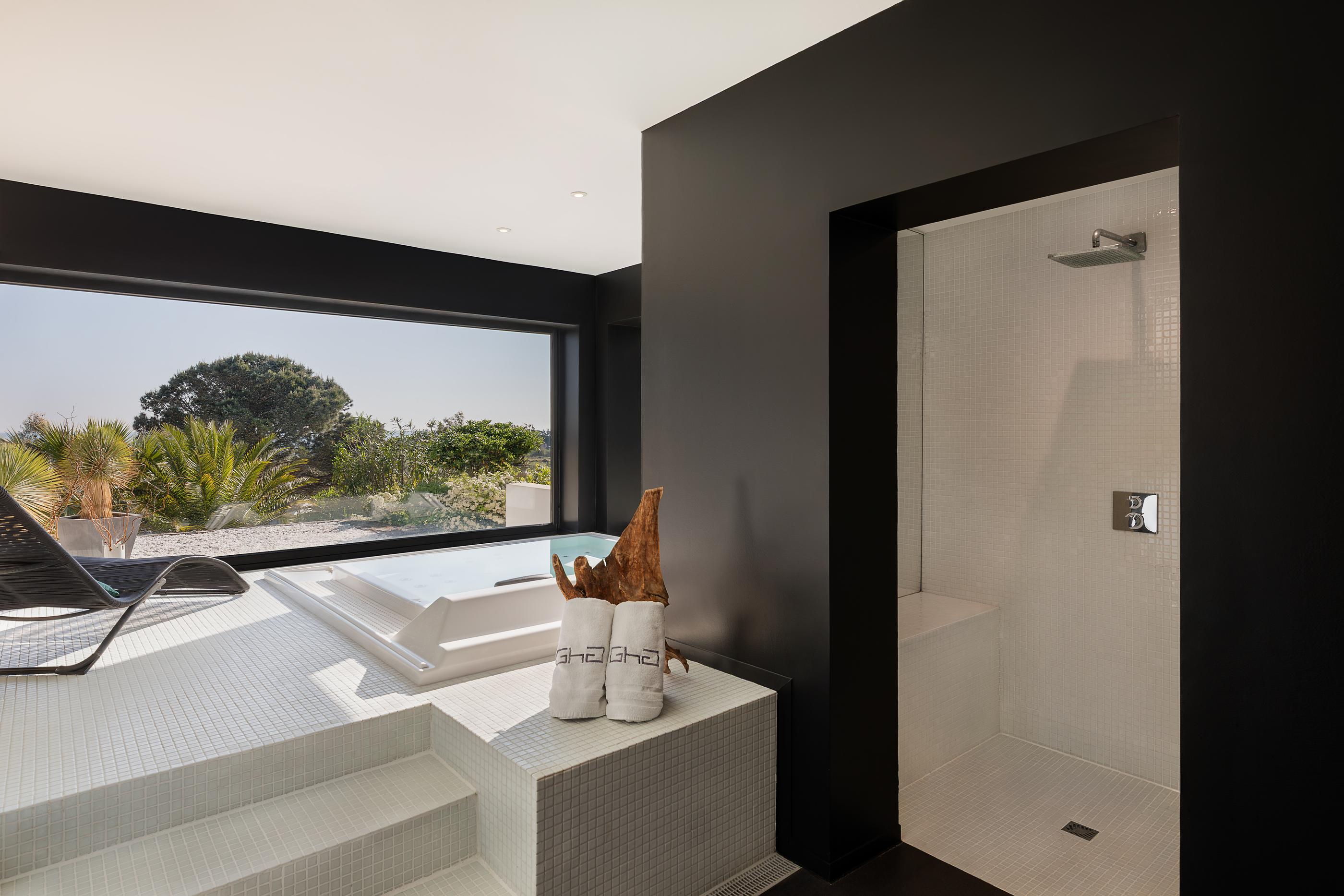 Salle de bain moderne avec baignoire, douche et vue sur un jardin tropical à travers une grande fenêtre